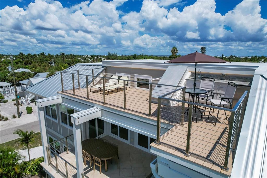 An elevated outdoor deck features lounge chairs, a dining set with an umbrella, and metal railings — 300 GASPARILLA STREET, BOCA GRANDE, FL