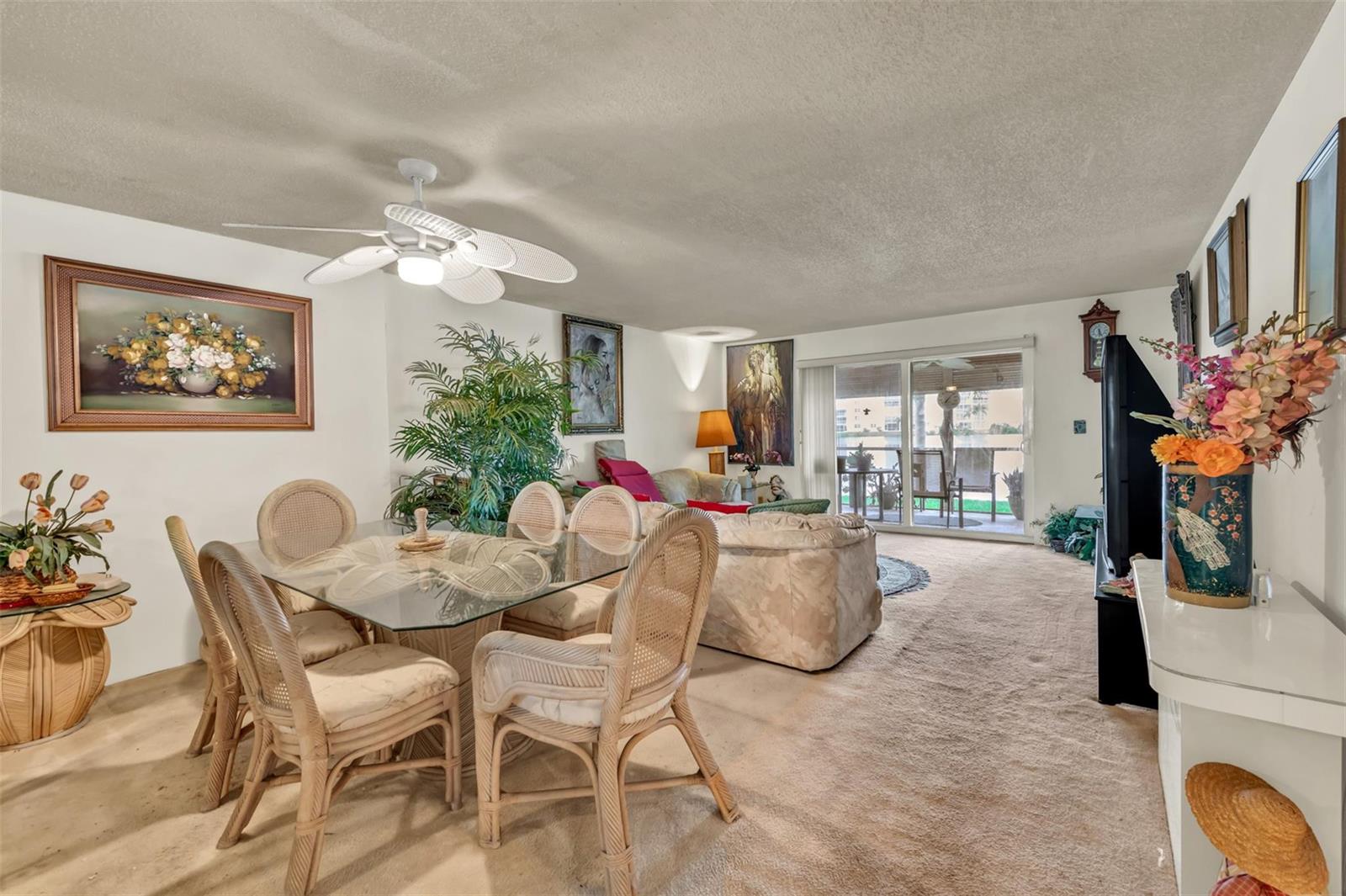A dining area with a glass table and wicker chairs sits beside a carpeted living room — 121 SE 3rd Avenue # 104, Dania Beach FL 33004, DANIA BEACH, FL