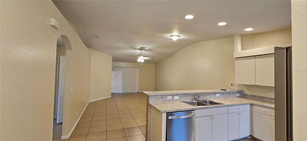 A kitchen with light-colored cabinets and countertops overlooks an open-concept living area with tile flooring — 1628 SW SANTA BARBARA PLACE, CAPE CORAL, FL
