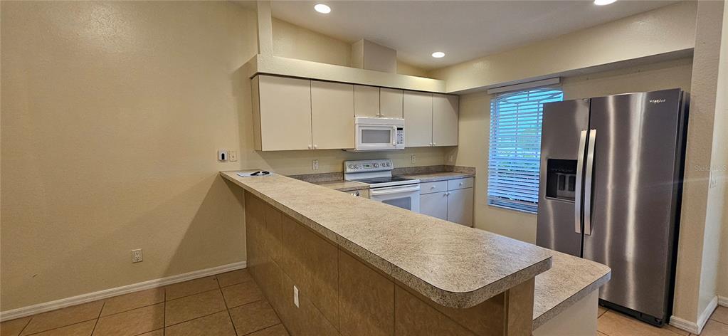 A kitchen features beige cabinets, laminate countertops, a breakfast bar, and stainless steel appliances — 1628 SW SANTA BARBARA PLACE, CAPE CORAL, FL