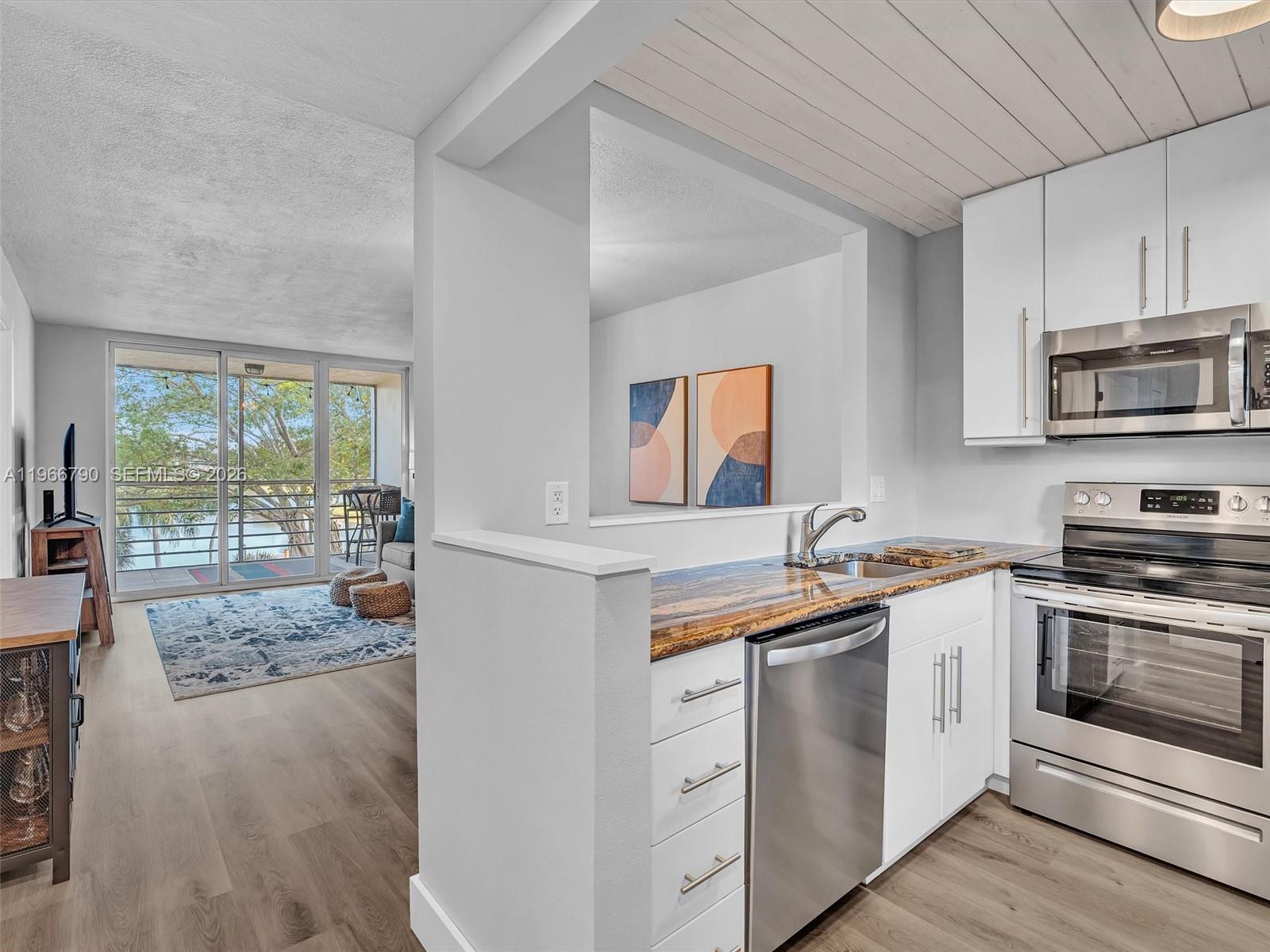 A kitchen with white cabinets and granite countertops overlooks a living area with a balcony — 9340 Lagoon Pl # 303, Davie FL 33324, DAVIE, FL