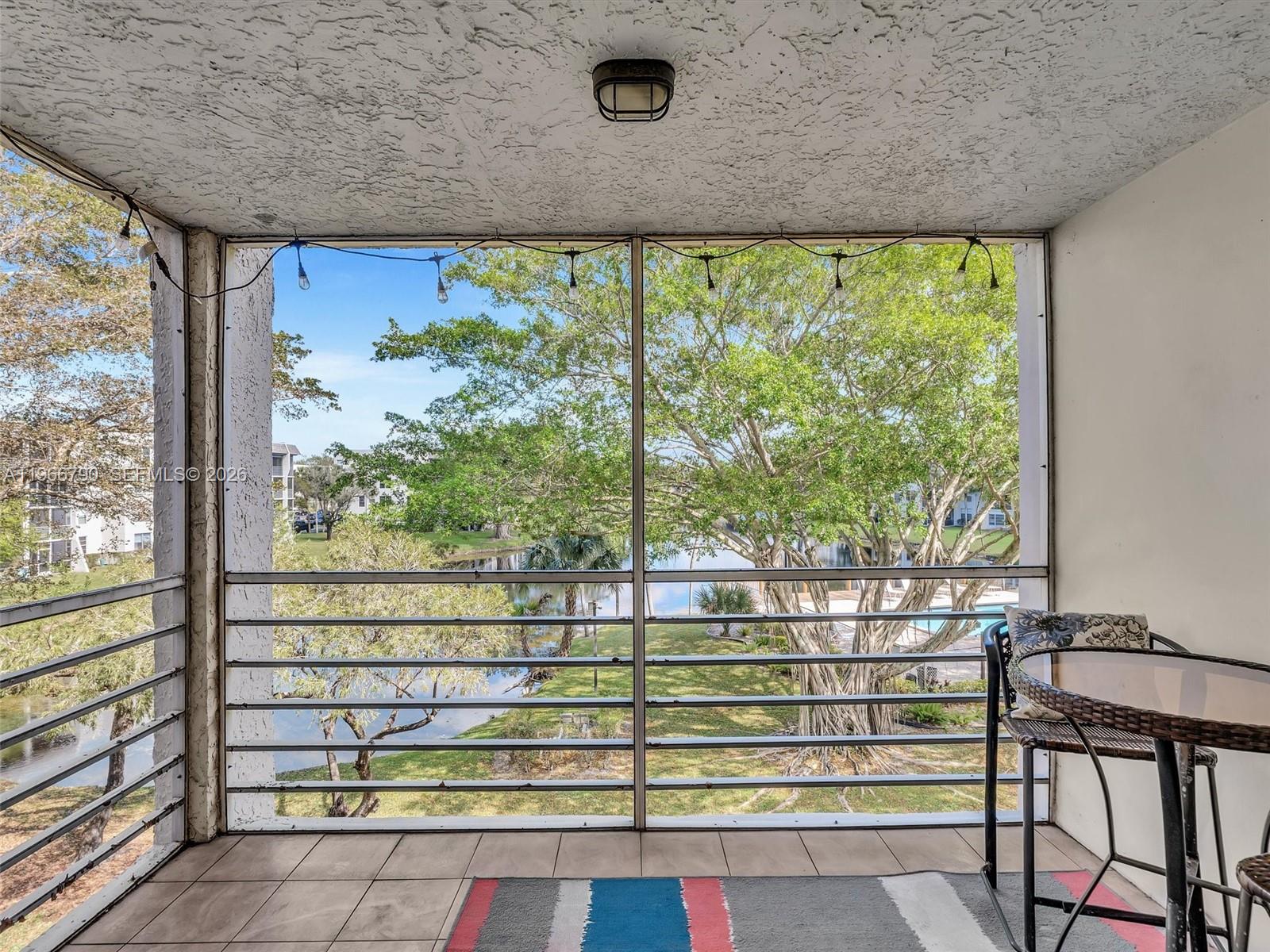 A screened-in balcony features tiled flooring, a small bistro table, and a view of trees — 9340 Lagoon Pl # 303, Davie FL 33324, DAVIE, FL