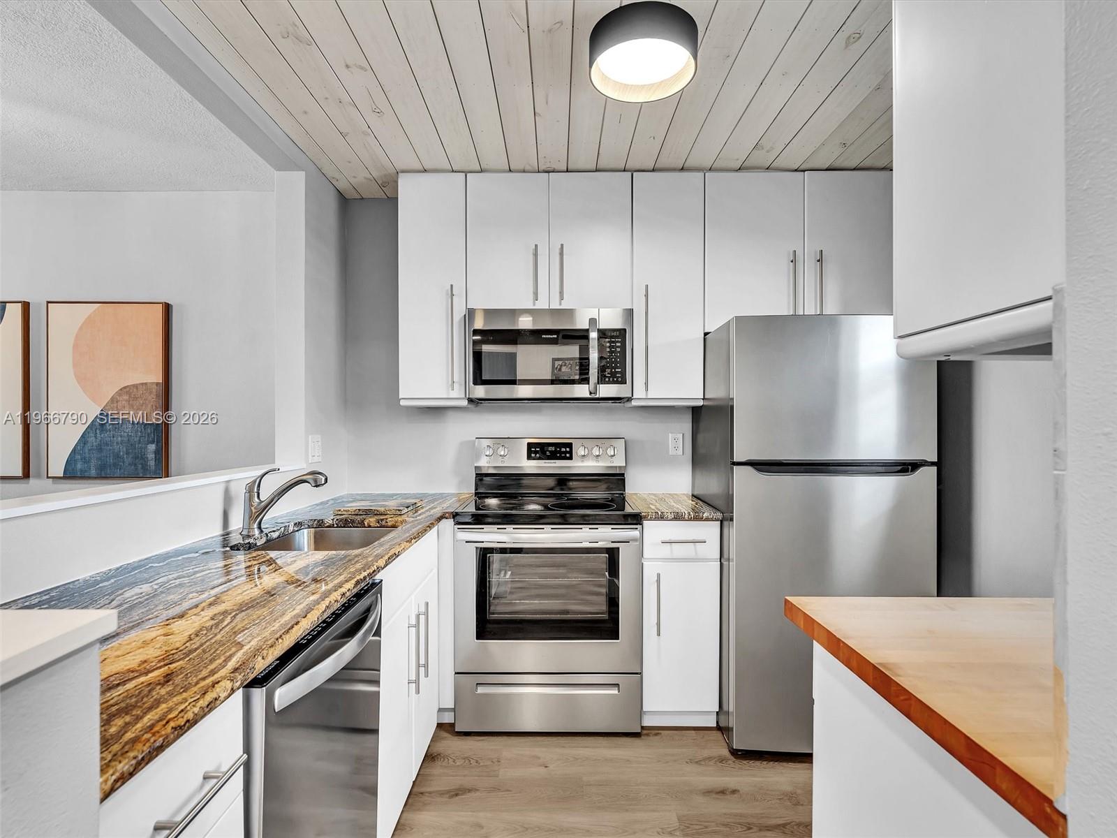A kitchen features white cabinets, stainless steel appliances, and a wood-plank ceiling — 9340 Lagoon Pl # 303, Davie FL 33324, DAVIE, FL