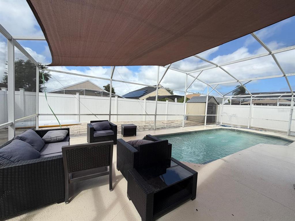 A screened-in patio features a swimming pool, outdoor wicker furniture, and a brown shade sail — 2558 E CHATMAN CIRCLE, KISSIMMEE, FL