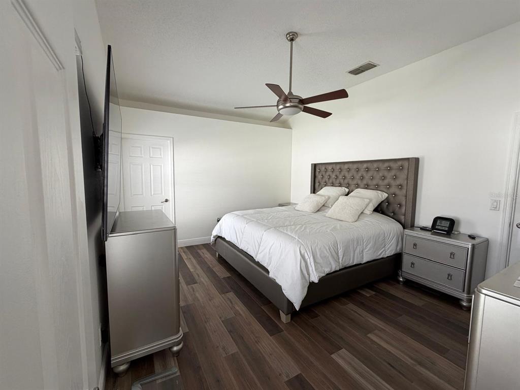 A bedroom features a tufted headboard, silver furniture, a ceiling fan, and wood-look flooring — 2558 E CHATMAN CIRCLE, KISSIMMEE, FL