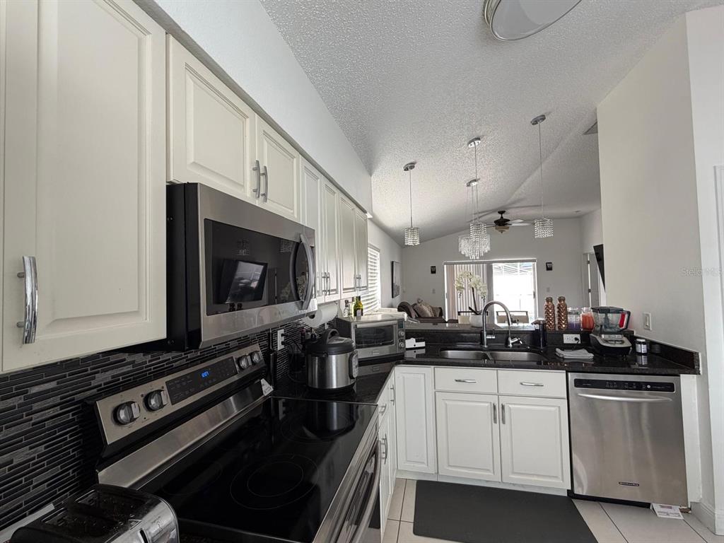 A kitchen features white cabinets, stainless steel appliances, and a dark tiled backsplash — 2558 E CHATMAN CIRCLE, KISSIMMEE, FL