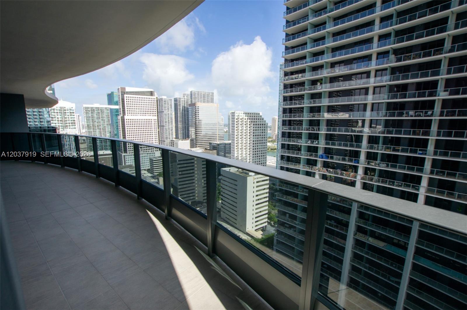 A curved balcony with a glass railing overlooks a dense city skyline of skyscrapers — 1000 Brickell Plaza # 2809, Miami FL 33131, MIAMI, FL