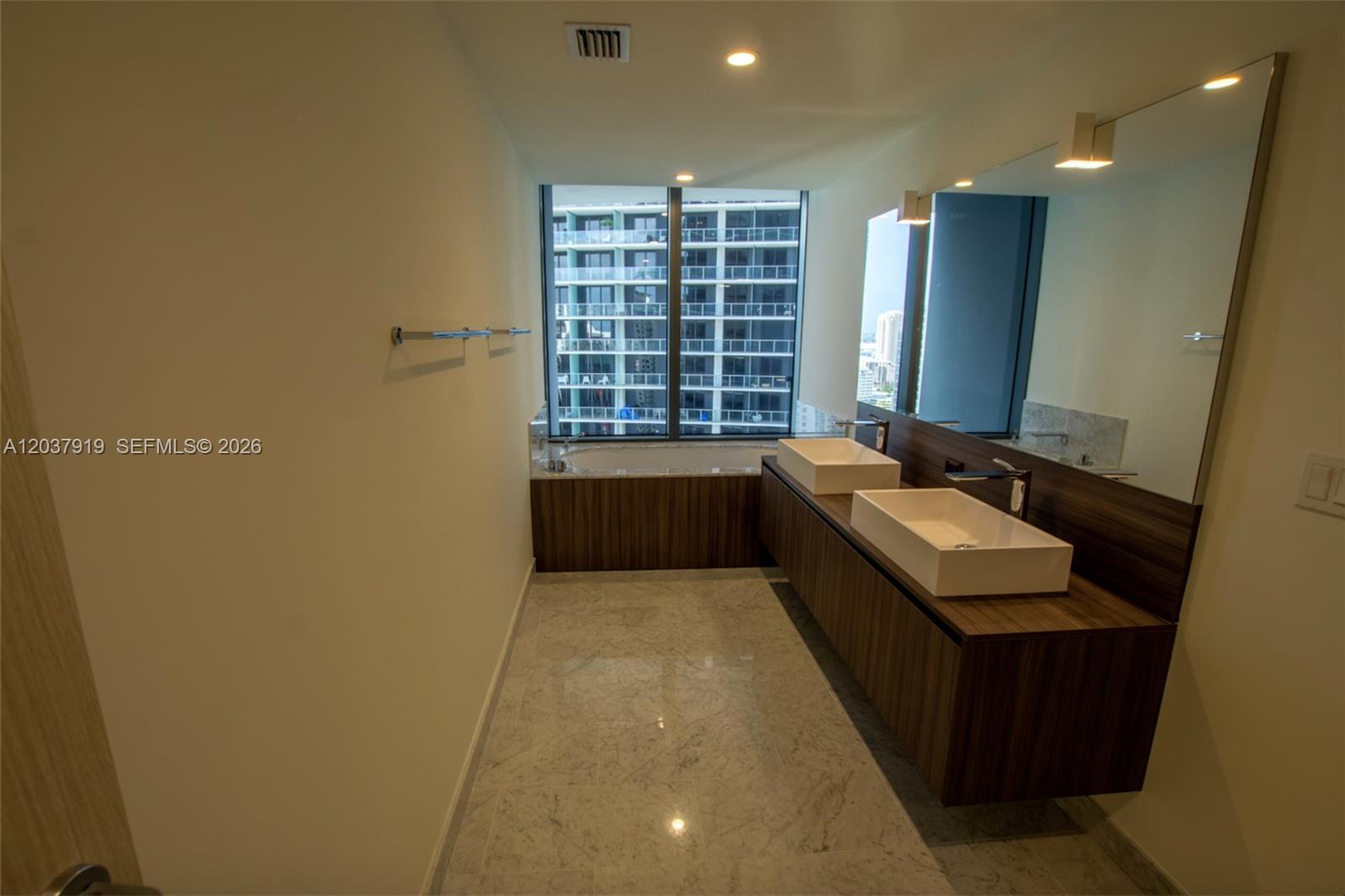 A modern bathroom features a double vanity, marble flooring, and a soaking tub by windows — 1000 Brickell Plaza # 2809, Miami FL 33131, MIAMI, FL