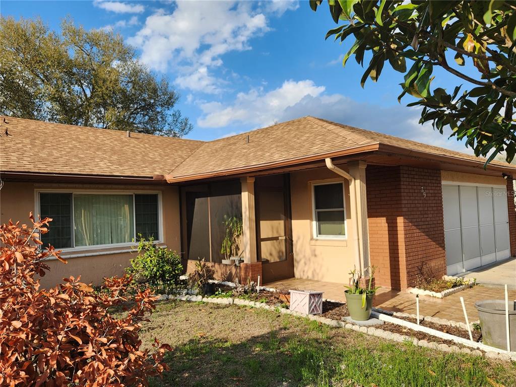 A single-story house with a tan stucco exterior, brick accents, and a screened front porch — 713 BEAR WAY, KISSIMMEE, FL