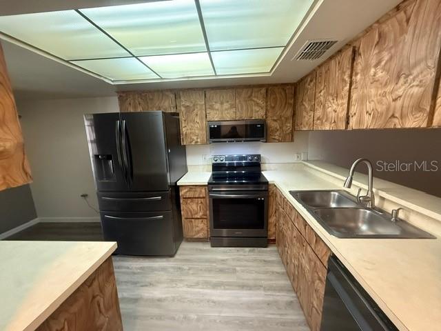 A kitchen features wood-grain cabinets, stainless steel appliances, and light-colored countertops under a drop ceiling — 2131 RIDGE ROAD S UNIT 74, LARGO, FL