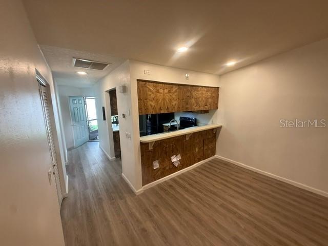 A kitchen with wood-patterned cabinets and a breakfast bar overlooks a room with wood-look flooring — 2131 RIDGE ROAD S UNIT 74, LARGO, FL