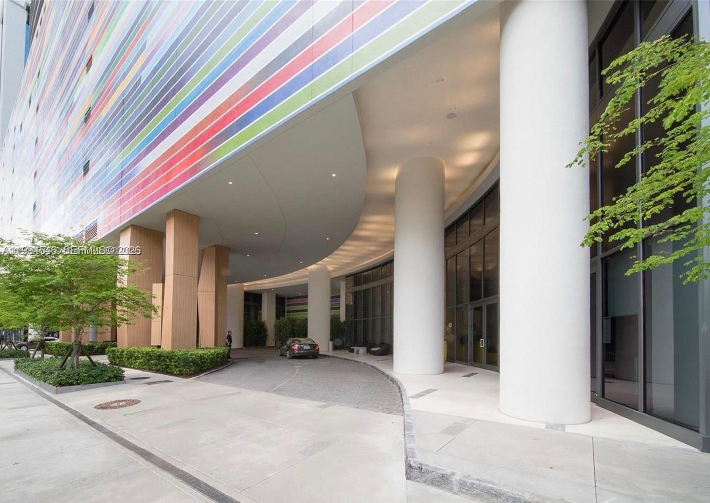 A curved driveway leads to a modern building entrance featuring colorful striped panels and columns — 55 SW 9th St # 1001, Miami FL 33130, MIAMI, FL