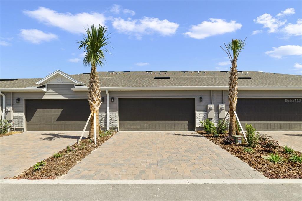 A row of townhome garages with paver driveways and two palm trees under a blue sky — 686 LOLA LANE, OVIEDO, FL
