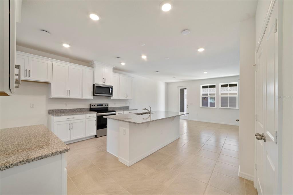 A kitchen features white cabinets, granite countertops, a central island, and tile flooring — 686 LOLA LANE, OVIEDO, FL