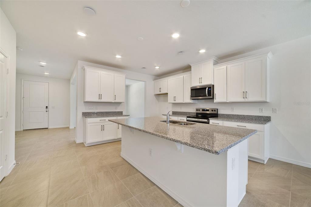 A kitchen with white cabinets, granite countertops, a center island, and light-colored tile flooring — 686 LOLA LANE, OVIEDO, FL