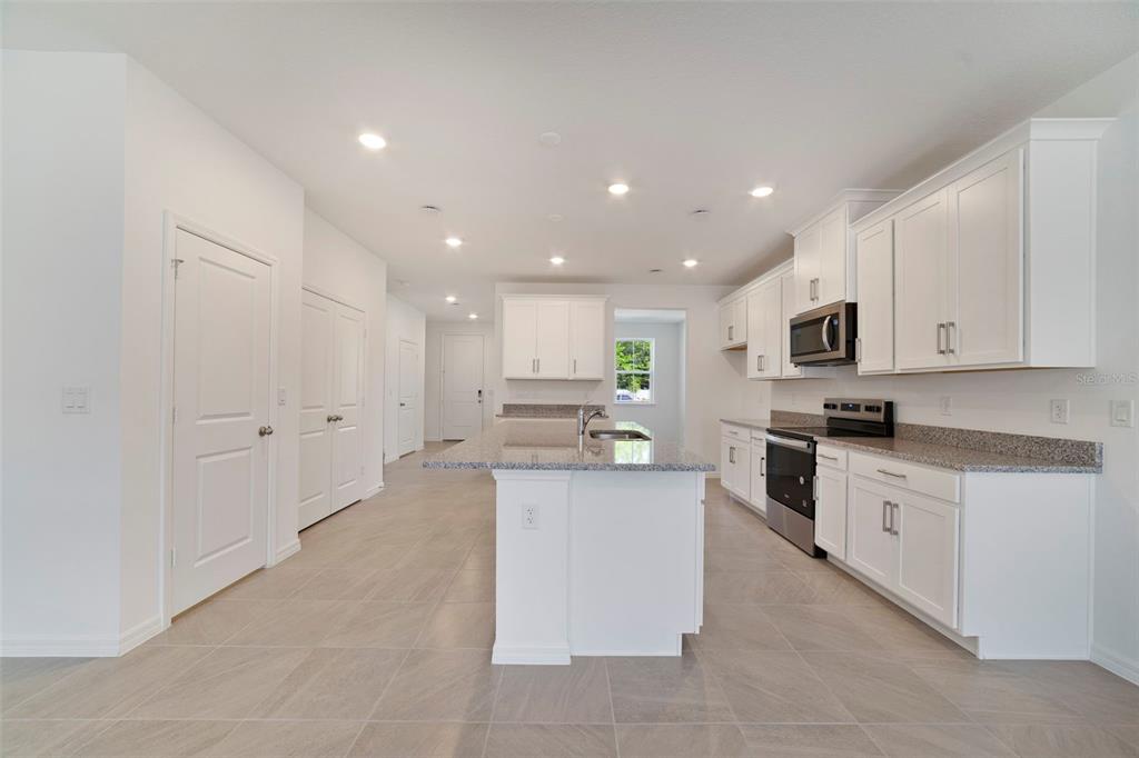 A bright kitchen features white cabinets, granite countertops, a center island, and tile flooring — 686 LOLA LANE, OVIEDO, FL