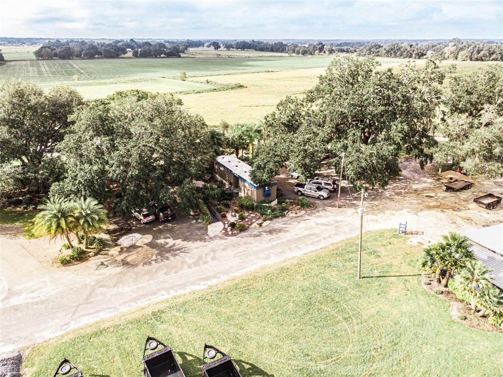An aerial view shows a house surrounded by large trees, parked vehicles, and open fields — 13494 N US HWY 301, OXFORD, FL