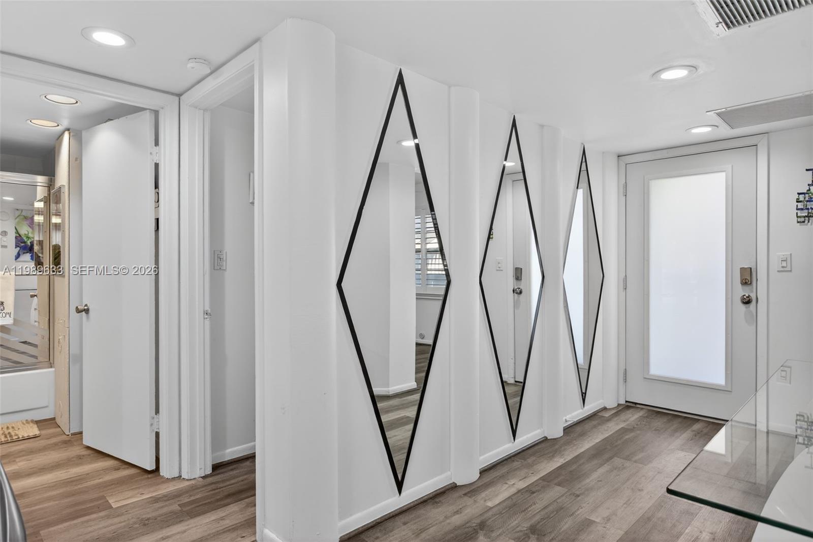 A hallway features wood-look flooring, three diamond-shaped wall mirrors, and white doors — 1802 Eleuthera POINT # C3, Coconut Creek FL 33066, COCONUT CREEK, FL