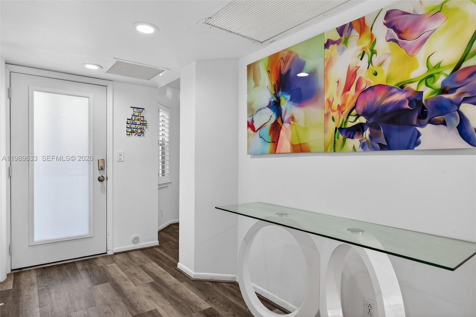 A white entryway features a glass console table, floral wall art, and wood-look flooring — 1802 Eleuthera POINT # C3, Coconut Creek FL 33066, COCONUT CREEK, FL