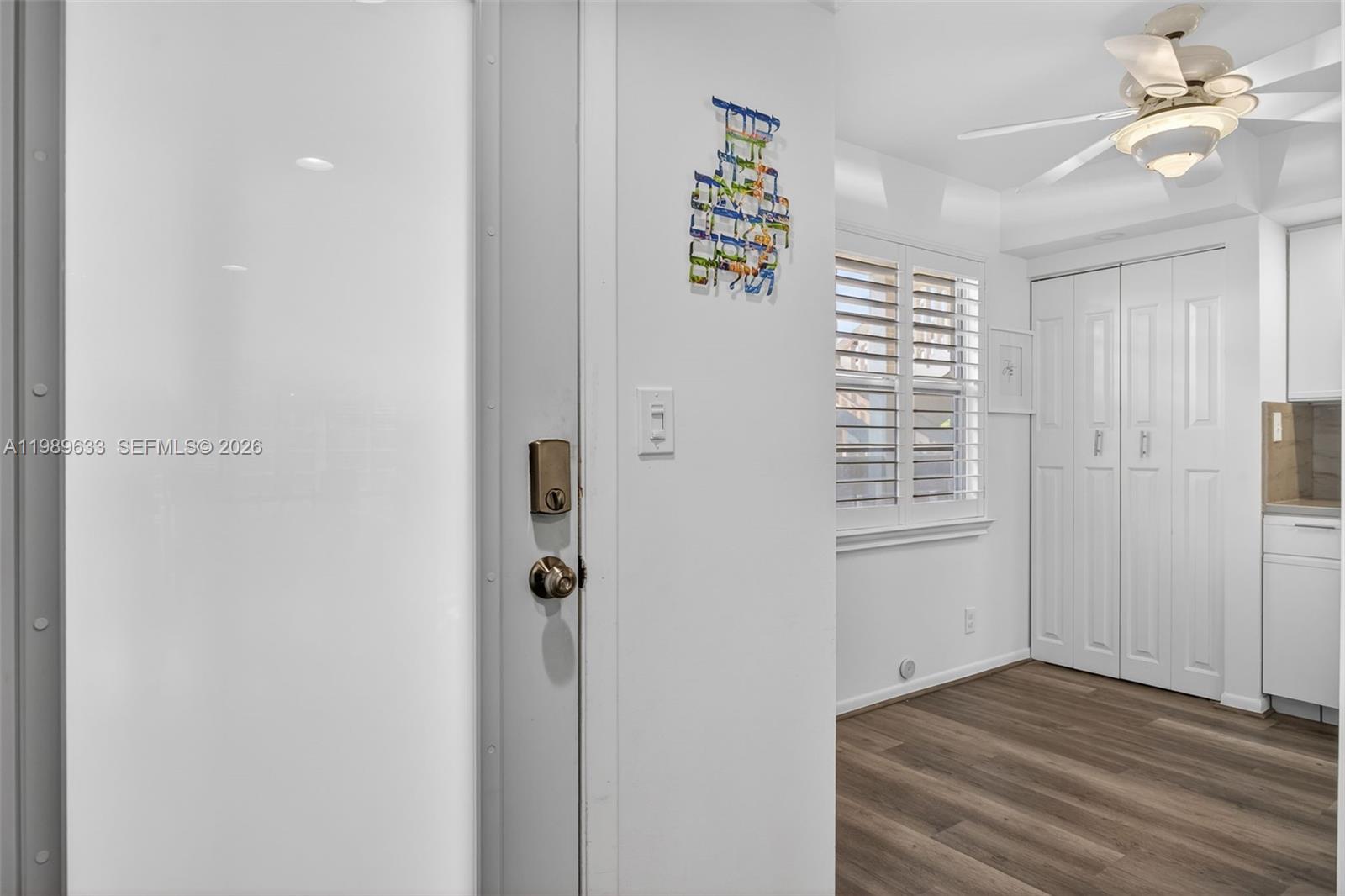 A white door opens into a room with wood-look flooring, white shutters, and a ceiling fan — 1802 Eleuthera POINT # C3, Coconut Creek FL 33066, COCONUT CREEK, FL