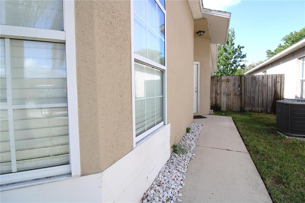 A concrete walkway runs along the side of a tan house with white-framed windows — 464 BRIAR BAY CIRCLE, ORLANDO, FL