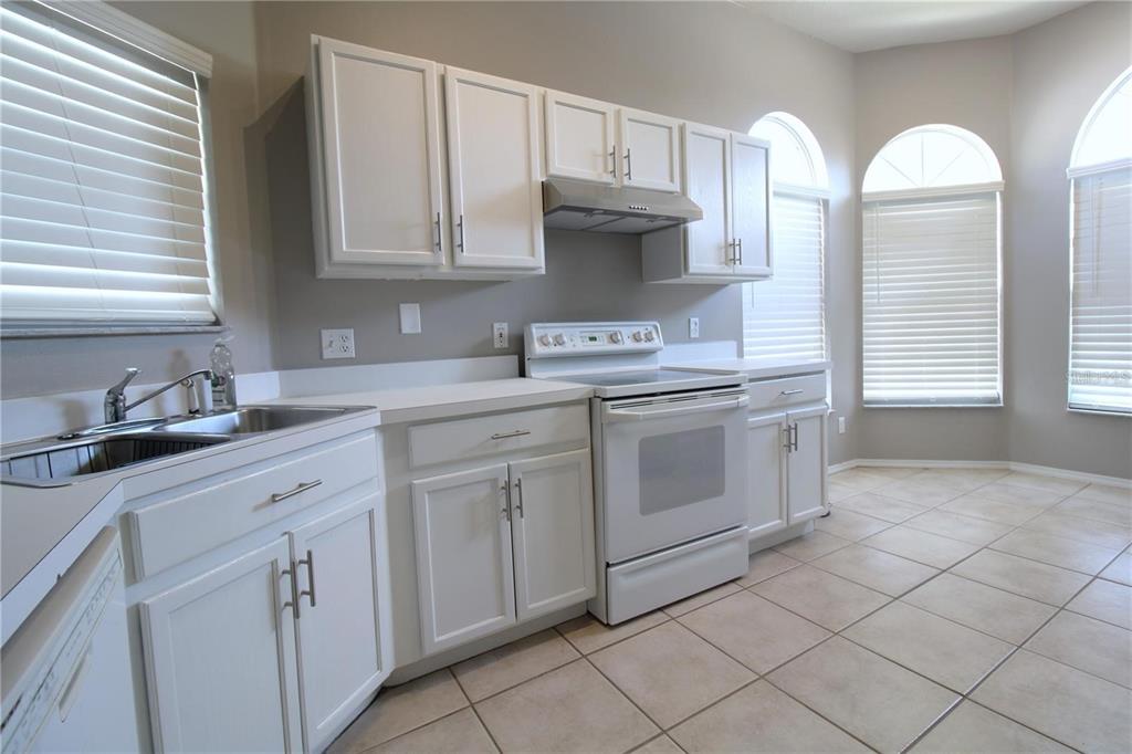 A kitchen features white cabinets, white appliances, a stainless steel sink, and light tile flooring — 464 BRIAR BAY CIRCLE, ORLANDO, FL