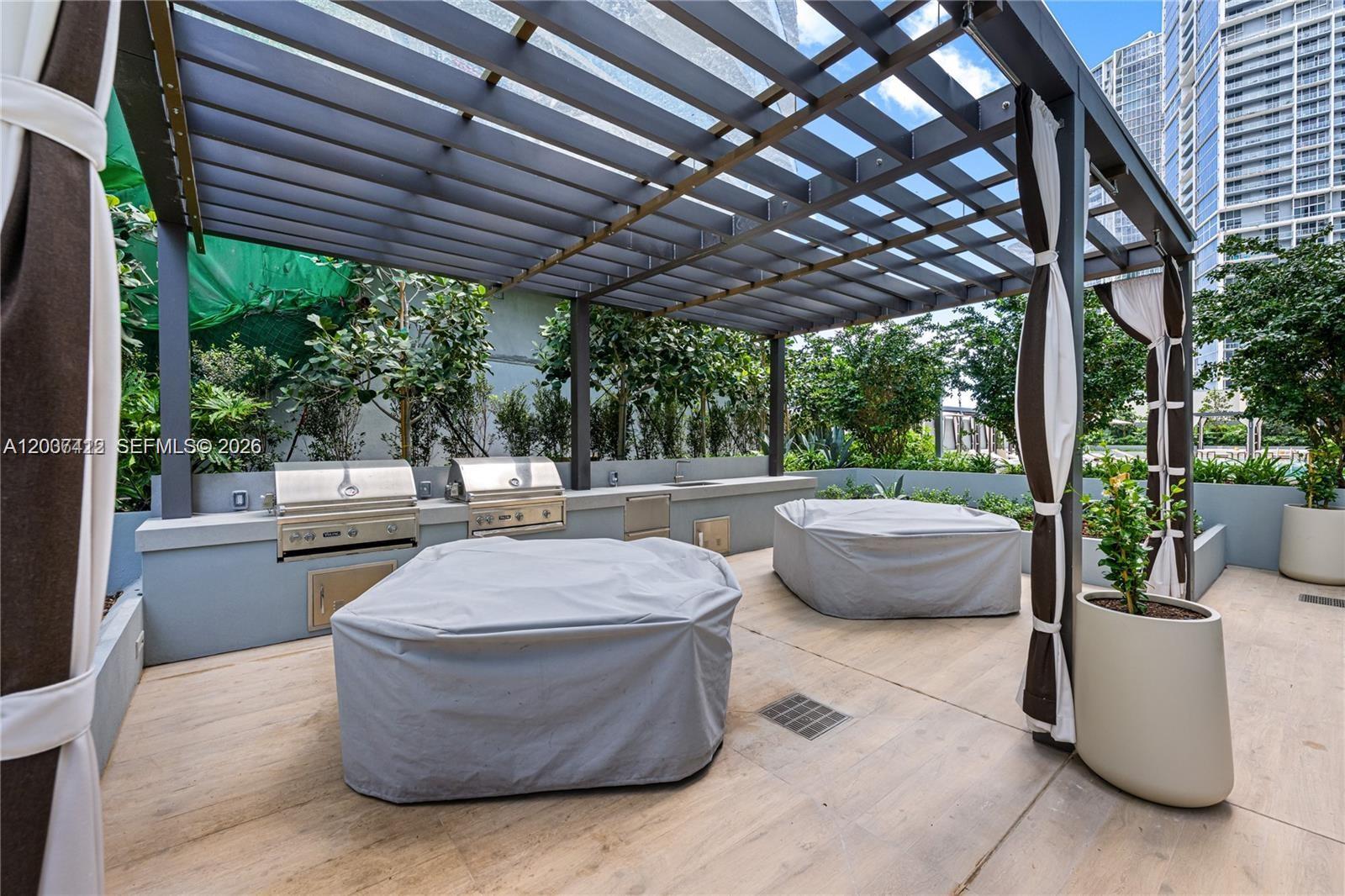An outdoor kitchen area features two stainless steel grills under a dark metal pergola — 77 SE 5th St # 1705, Miami FL 33131, MIAMI, FL