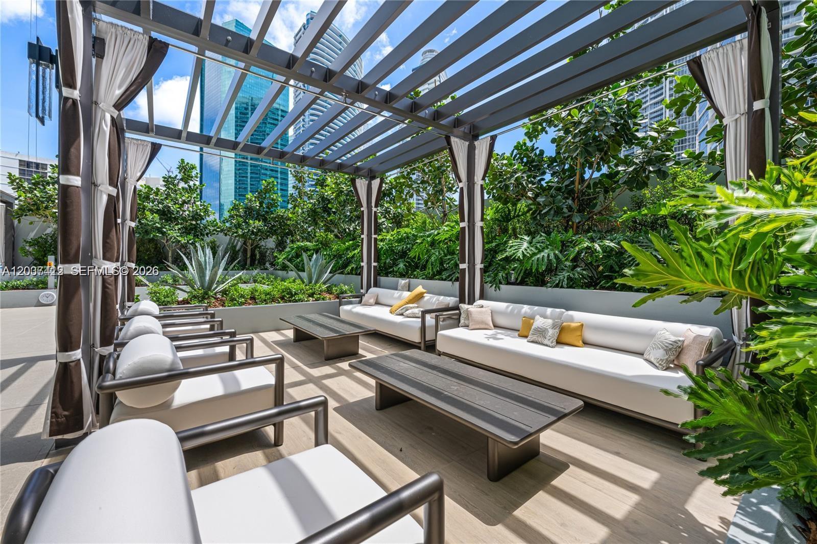 An outdoor lounge area features a pergola, white sofas, and coffee tables on a patio — 77 SE 5th St # 1705, Miami FL 33131, MIAMI, FL