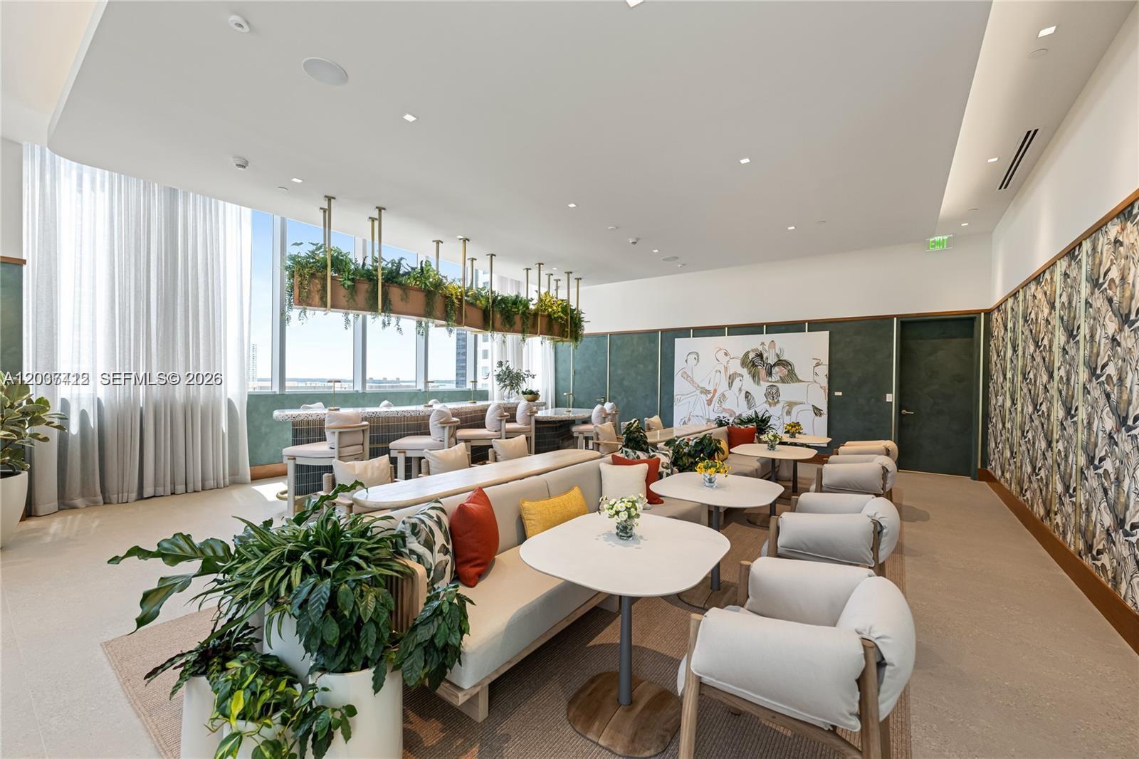 A modern lounge area features a long sofa, small tables, armchairs, and hanging greenery — 77 SE 5th St # 1705, Miami FL 33131, MIAMI, FL