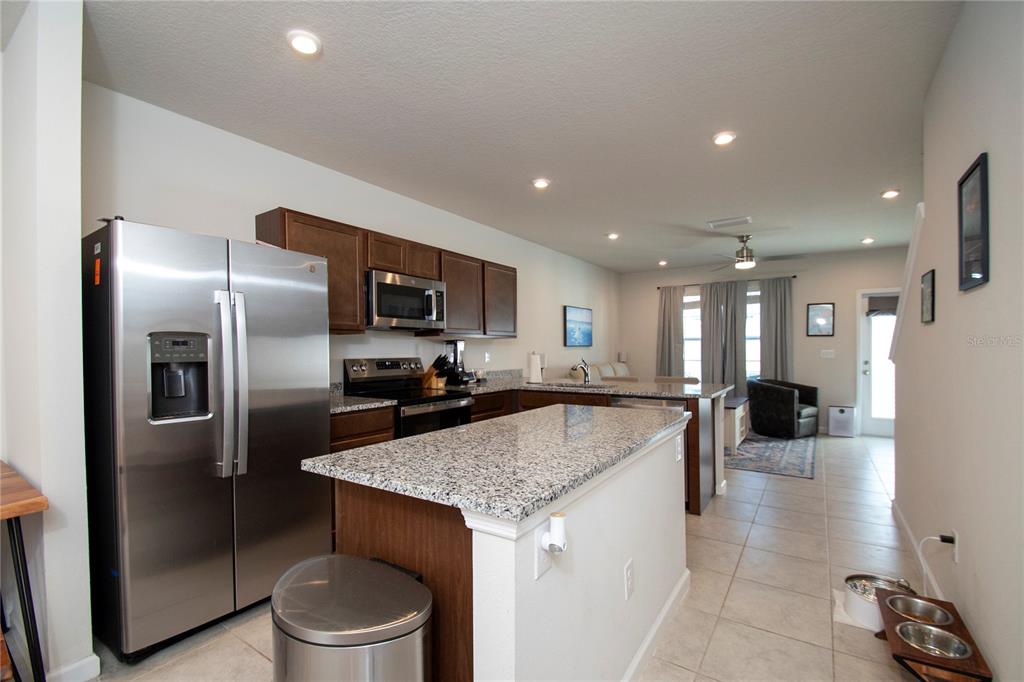 A kitchen with stainless steel appliances, granite countertops, and dark wood cabinets opens to a living area — 4660 OLD BLUSH STREET, BRADENTON, FL