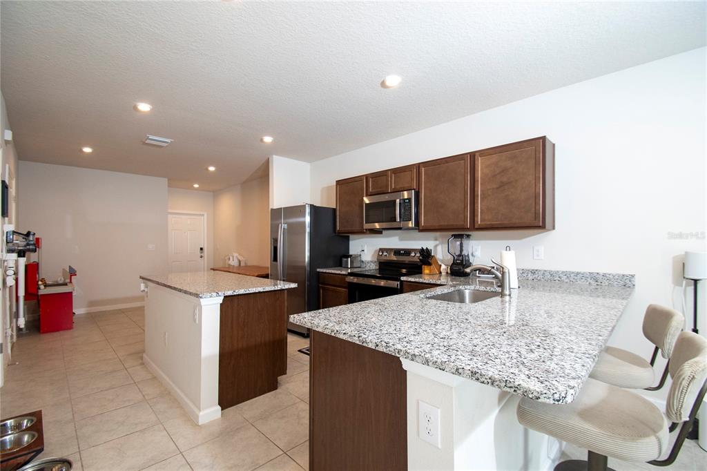 A kitchen features dark wood cabinets, granite countertops, stainless steel appliances, and a breakfast bar — 4660 OLD BLUSH STREET, BRADENTON, FL