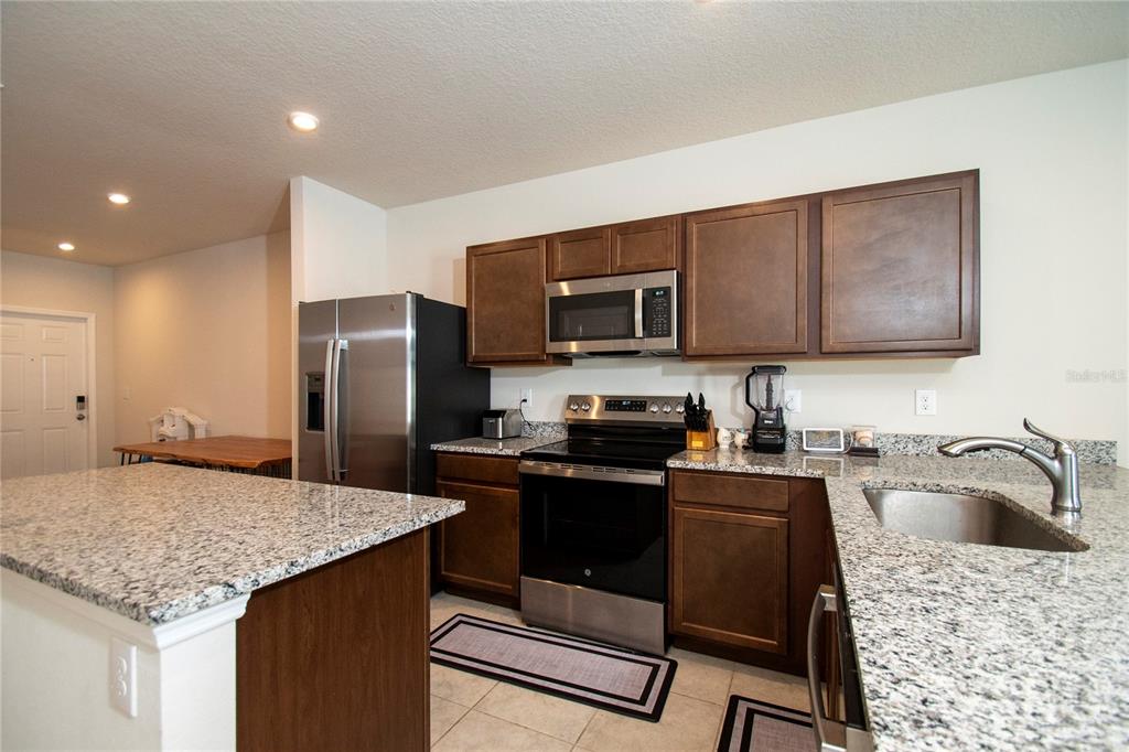 A kitchen features dark wood cabinets, granite countertops, stainless steel appliances, and a center island — 4660 OLD BLUSH STREET, BRADENTON, FL
