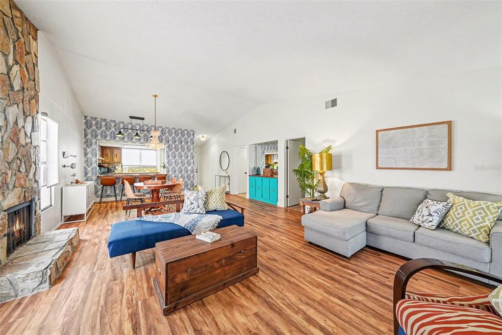 A living room with a stone fireplace, wood-look flooring, and an adjacent dining area — 9990 EAGLES POINT CIRCLE UNIT 4, PORT RICHEY, FL