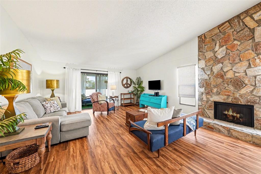 A living room features wood-look flooring, a stone fireplace, and a blue accent cabinet — 9990 EAGLES POINT CIRCLE UNIT 4, PORT RICHEY, FL