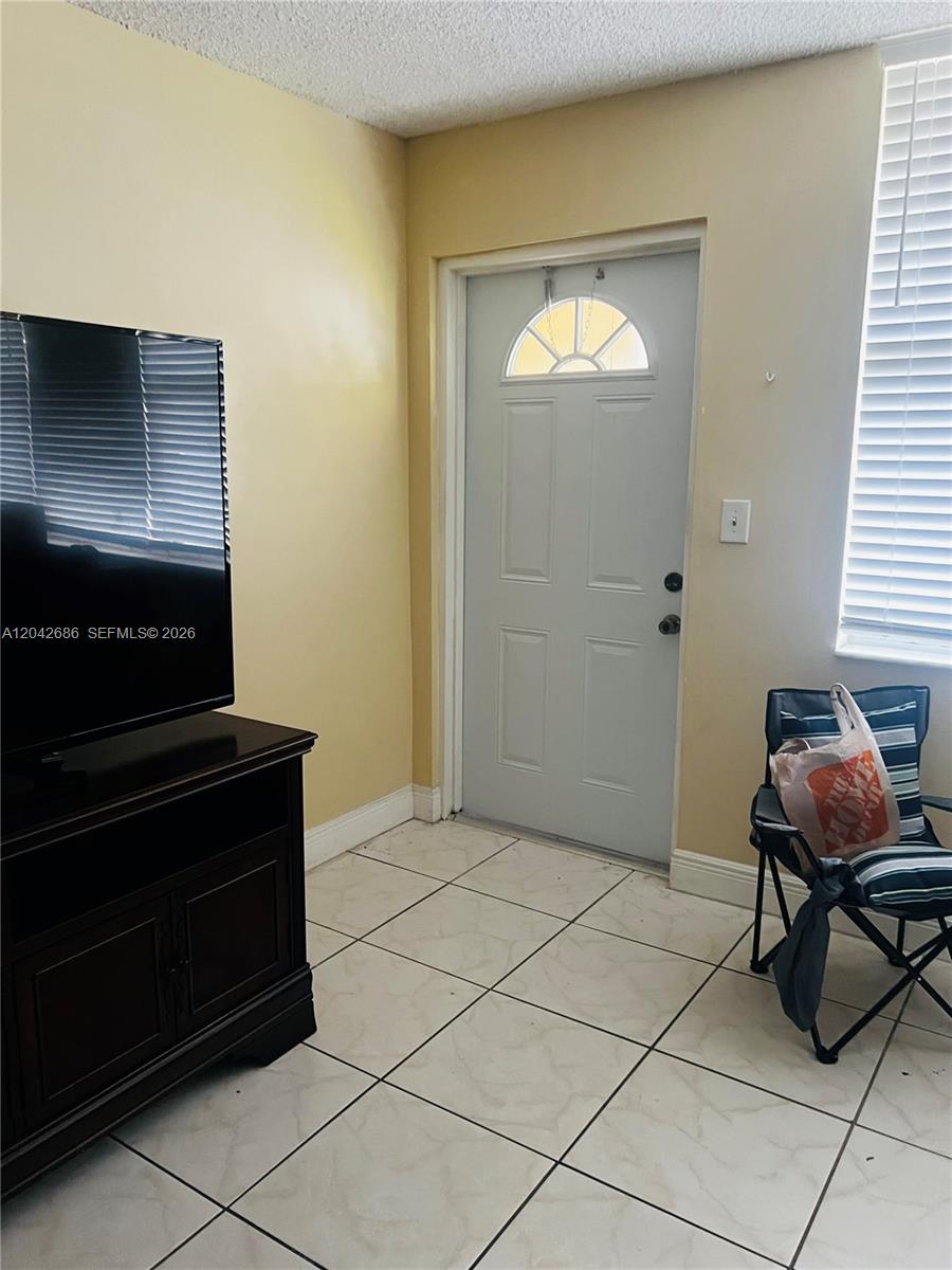 A room with light-colored tile flooring, a television on a stand, and an exterior door — SUNRISE, FL