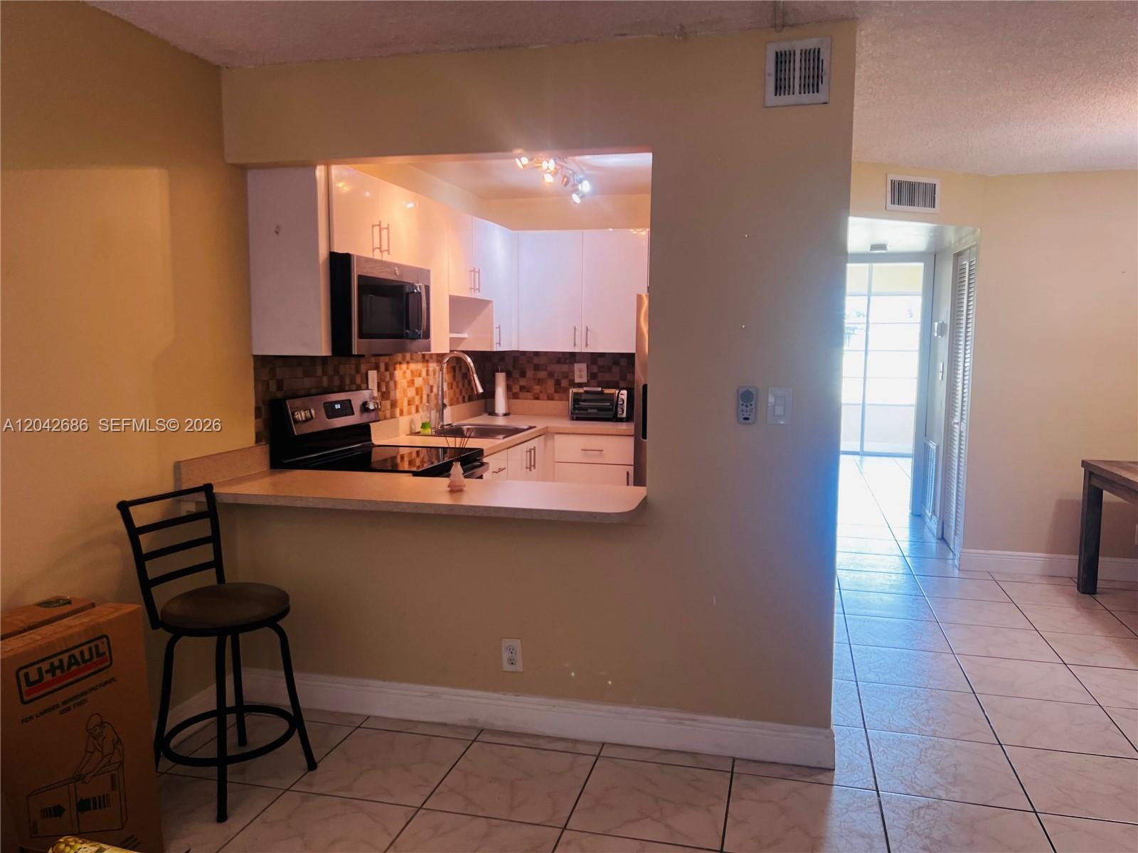 A kitchen with white cabinets and a breakfast bar opens into a tiled living area — SUNRISE, FL