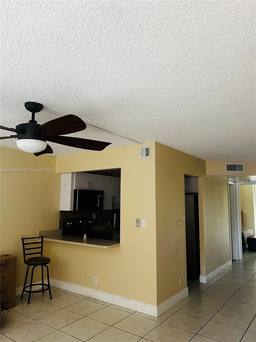 A kitchen pass-through window overlooks a tiled dining area with a ceiling fan — SUNRISE, FL