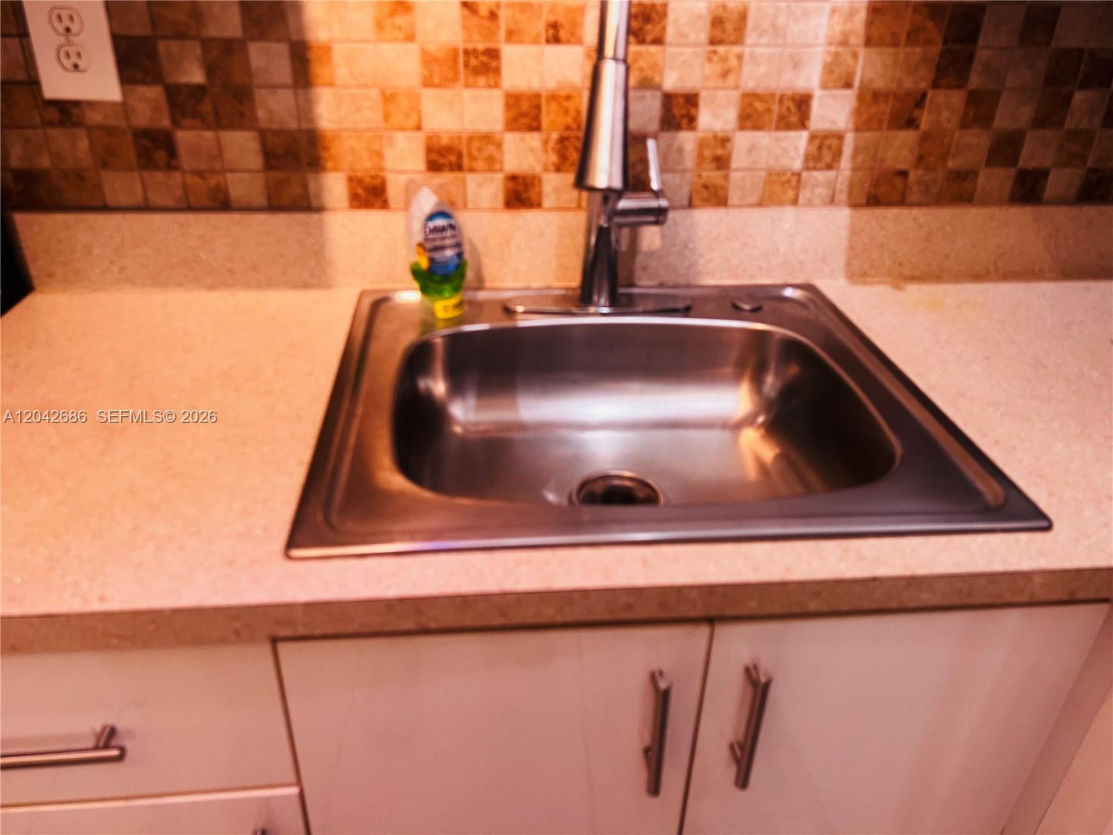 A stainless steel kitchen sink with a faucet sits in a countertop with tiled backsplash — SUNRISE, FL