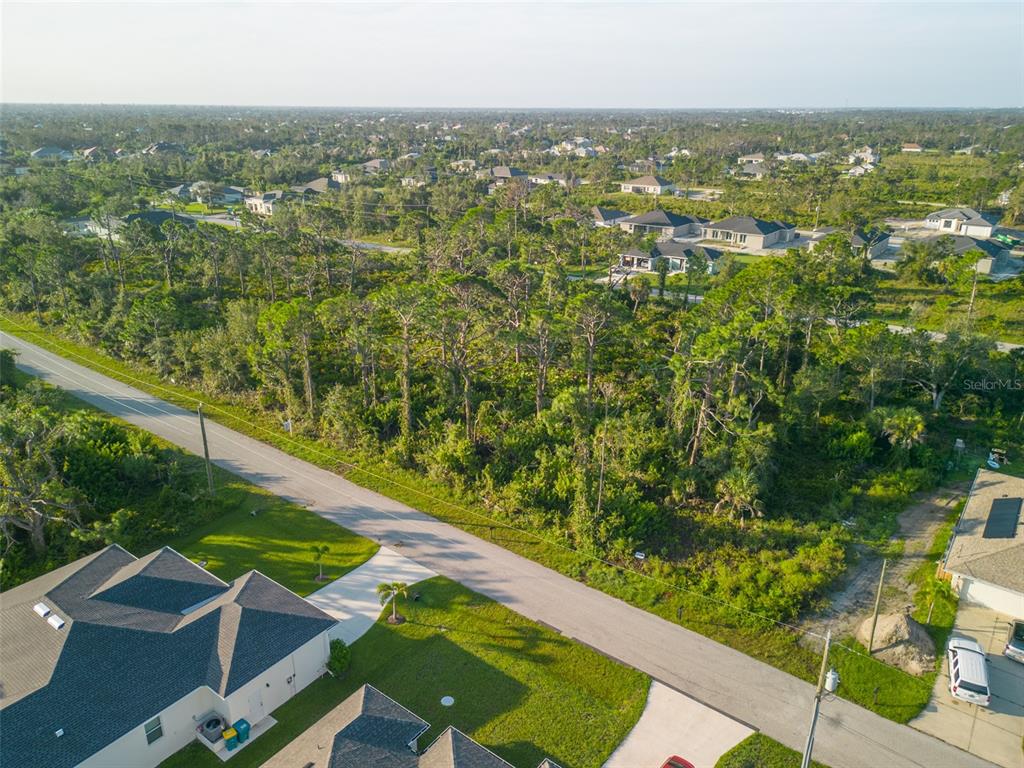 An aerial view shows a vacant, wooded lot situated between residential houses and a paved road — 13375 YAGER LANE, PORT CHARLOTTE, FL