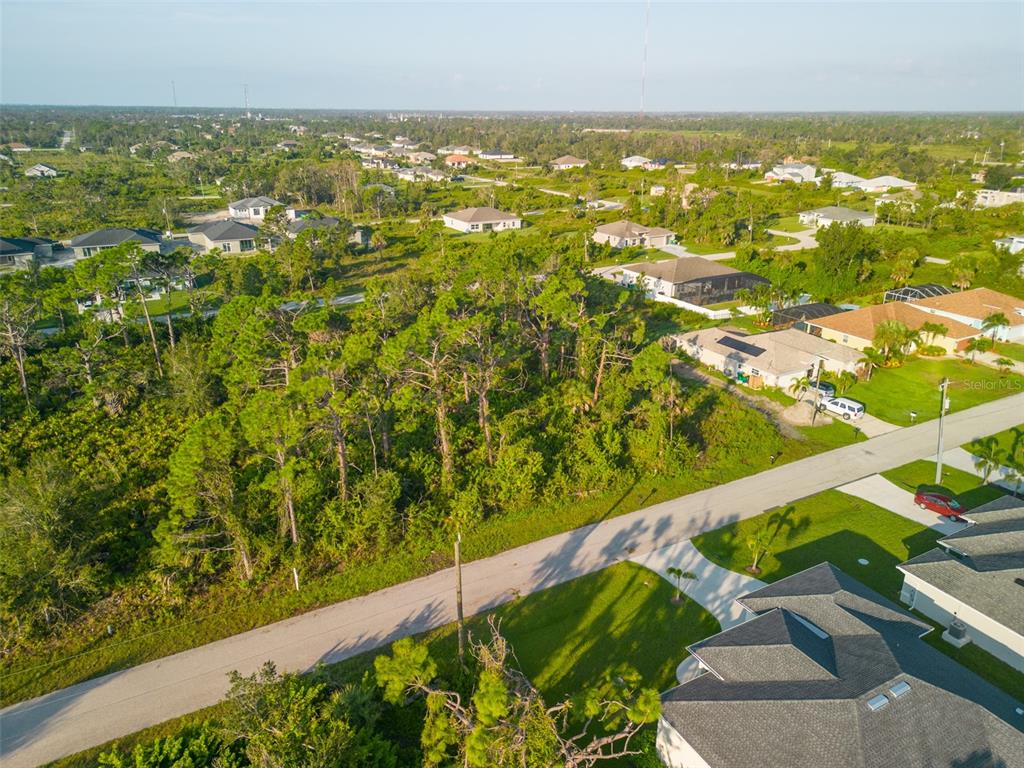 An aerial view shows a vacant, wooded lot situated between suburban houses and a paved road — 13375 YAGER LANE, PORT CHARLOTTE, FL