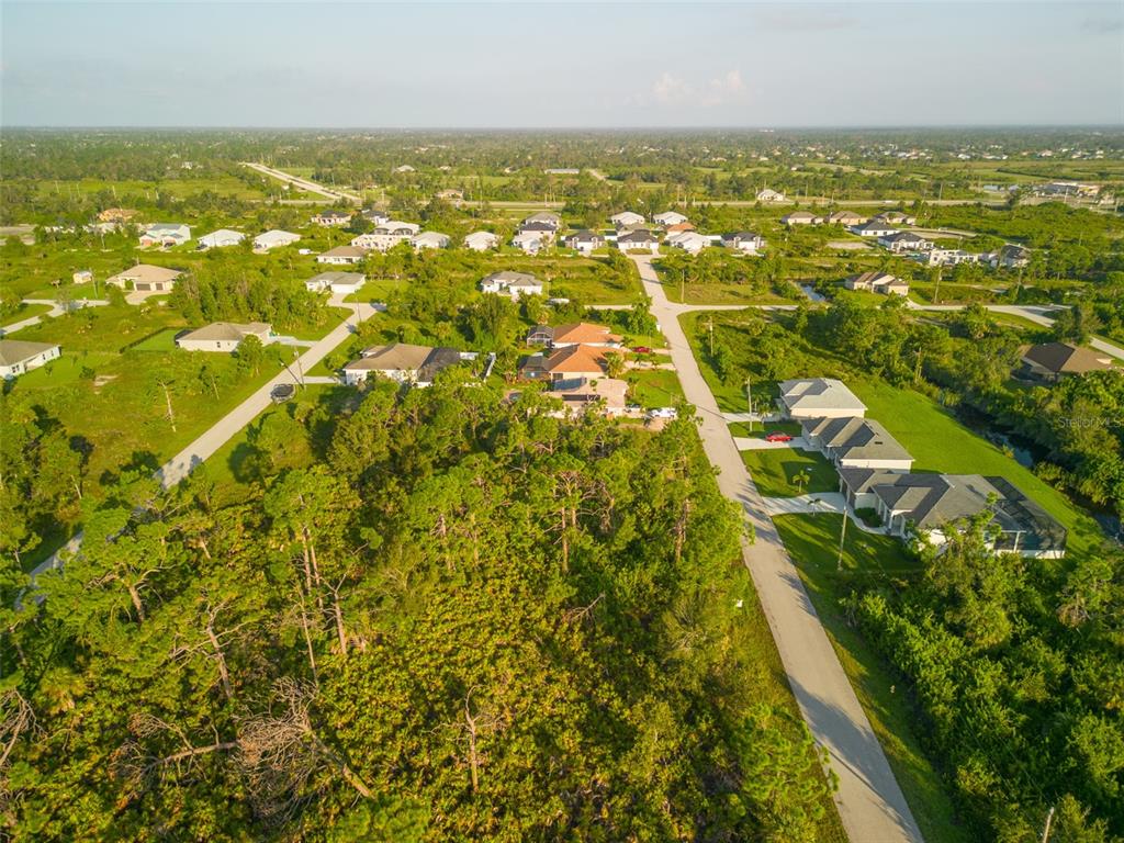 An aerial view shows a residential neighborhood with scattered houses surrounded by dense, wooded vegetation — 13375 YAGER LANE, PORT CHARLOTTE, FL