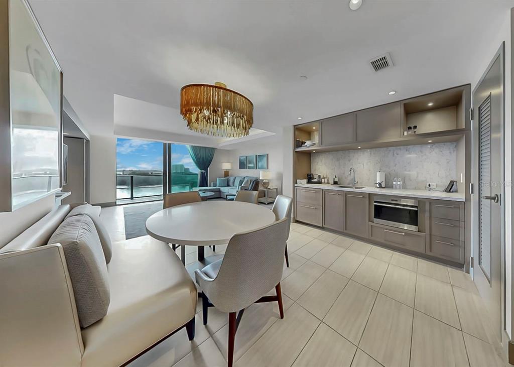 A modern kitchen and dining area with a round table, banquette seating, and balcony view — 691 S GULFVIEW BOULEVARD UNIT 1410, CLEARWATER BEACH, FL