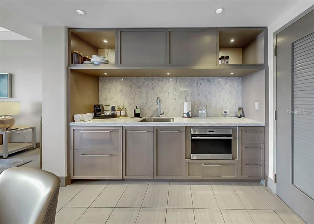 A modern wet bar features gray cabinetry, marble-style countertops, a sink, and built-in appliances — 691 S GULFVIEW BOULEVARD UNIT 1410, CLEARWATER BEACH, FL