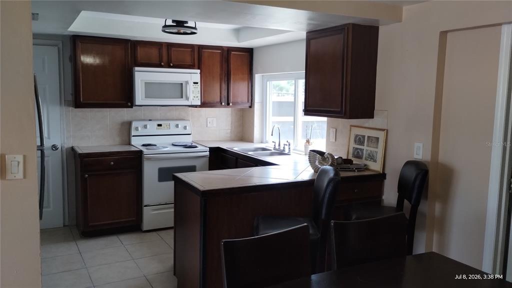 A kitchen with dark wood cabinets, white appliances, tile countertops, and a breakfast bar — 3637 WINDER DRIVE, HOLIDAY, FL