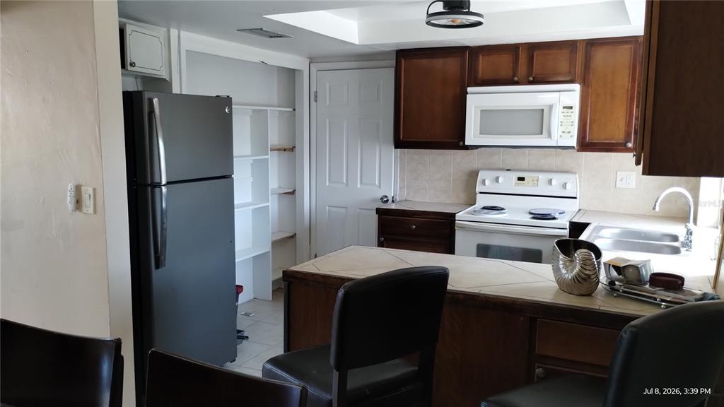 A kitchen features dark wood cabinets, a black refrigerator, white appliances, and a tiled counter — 3637 WINDER DRIVE, HOLIDAY, FL