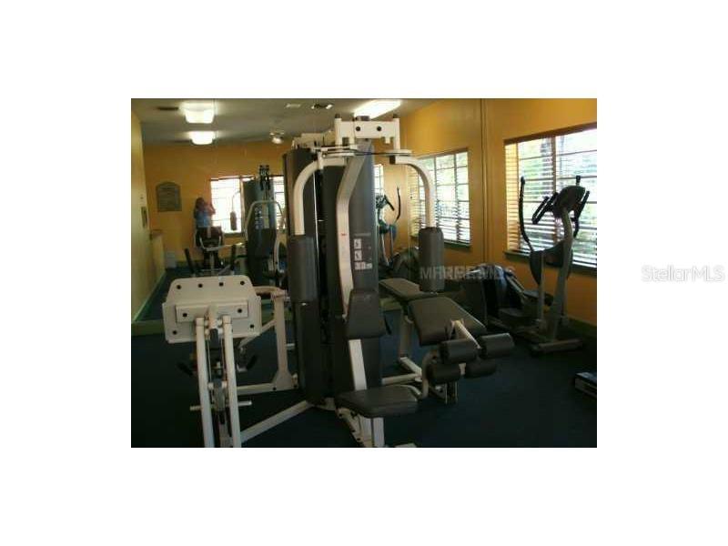 A gym room features a multi-station weight machine, exercise equipment, and windows with blinds — 5620 PINNACLE HEIGHTS CIRCLE UNIT 303, TAMPA, FL