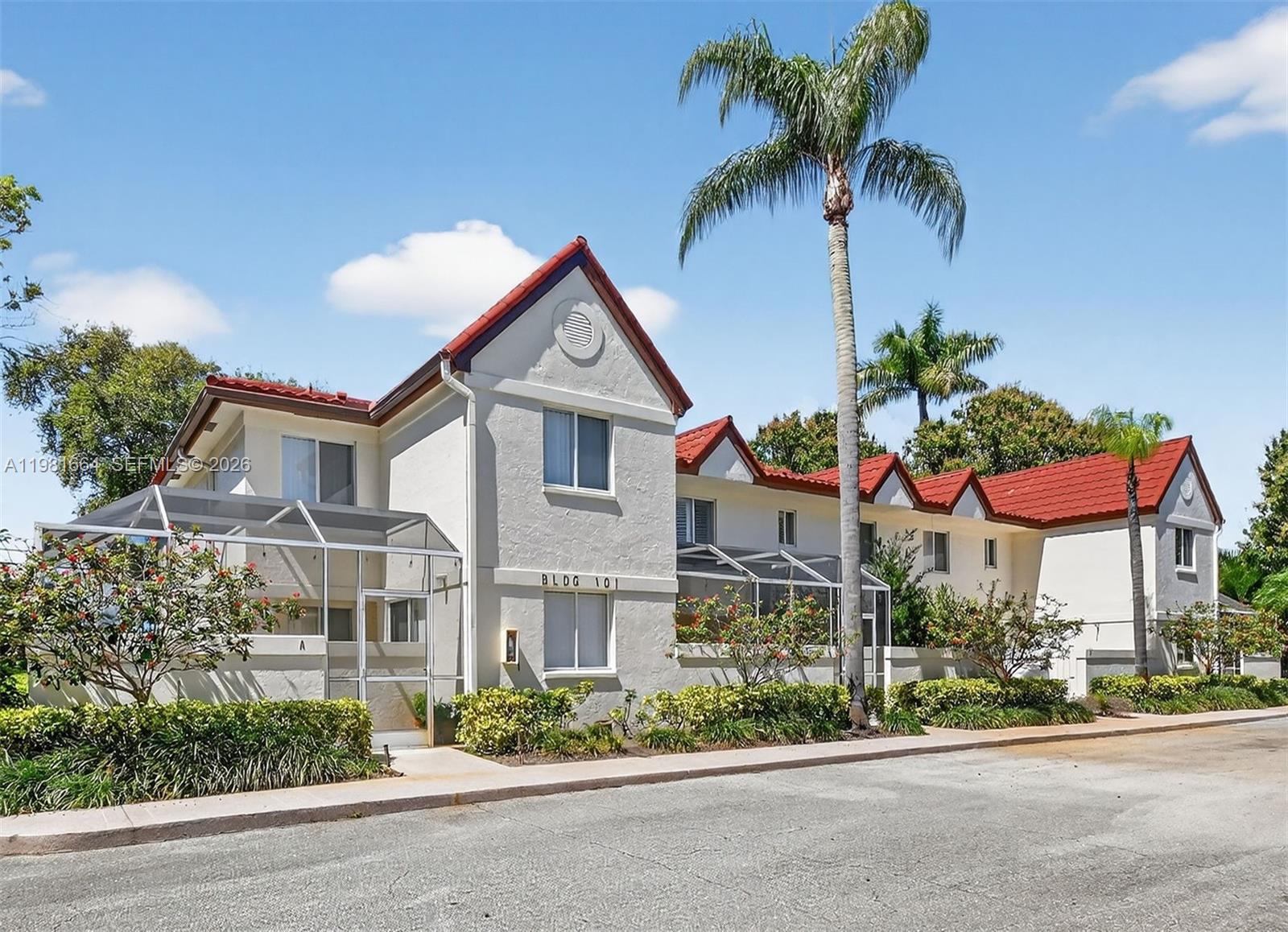 A two-story building with a red tile roof and screened-in patios sits under a palm tree — 101 E Half Moon Cir # B, Hypoluxo FL 33462, HYPOLUXO, FL