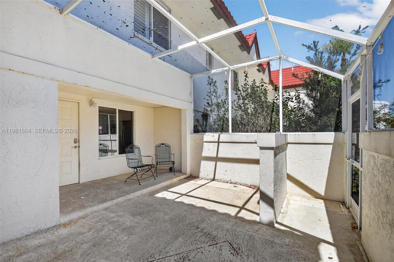 A screened-in patio features a concrete floor, two metal chairs, and a white door — 101 E Half Moon Cir # B, Hypoluxo FL 33462, HYPOLUXO, FL
