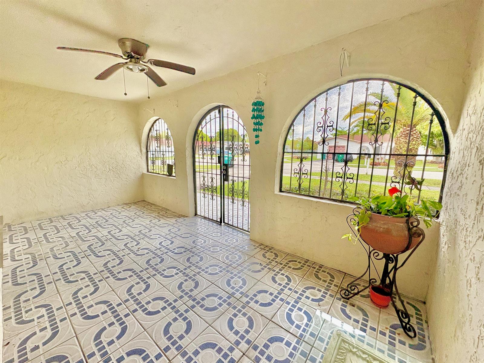 A covered patio features patterned tile flooring, a ceiling fan, and arched wrought-iron security gates — 10774 SW 175th Terrace, Miami FL 33157, MIAMI, FL