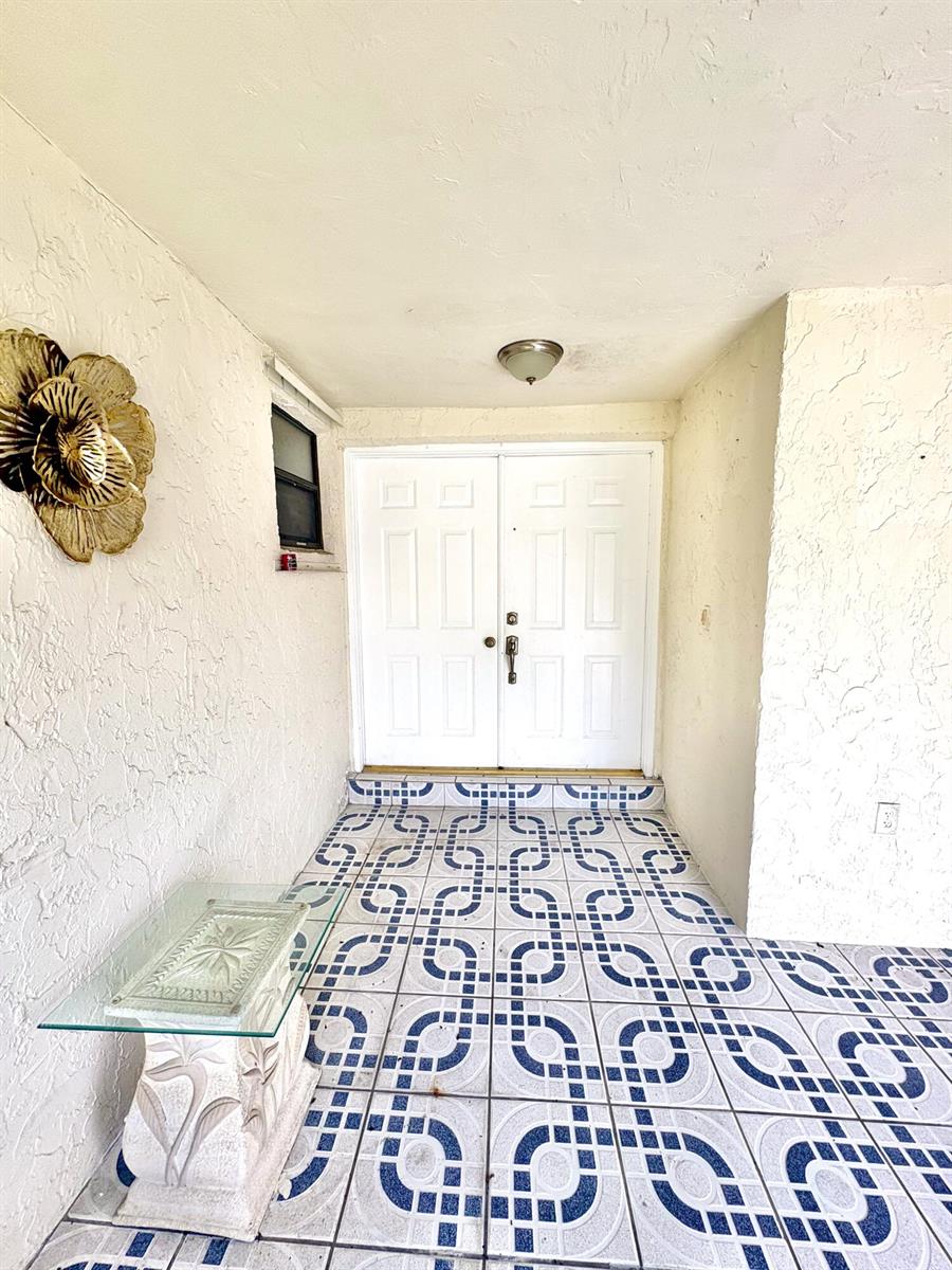 A covered entryway features white double doors, patterned blue and white tile, and stucco walls — 10774 SW 175th Terrace, Miami FL 33157, MIAMI, FL